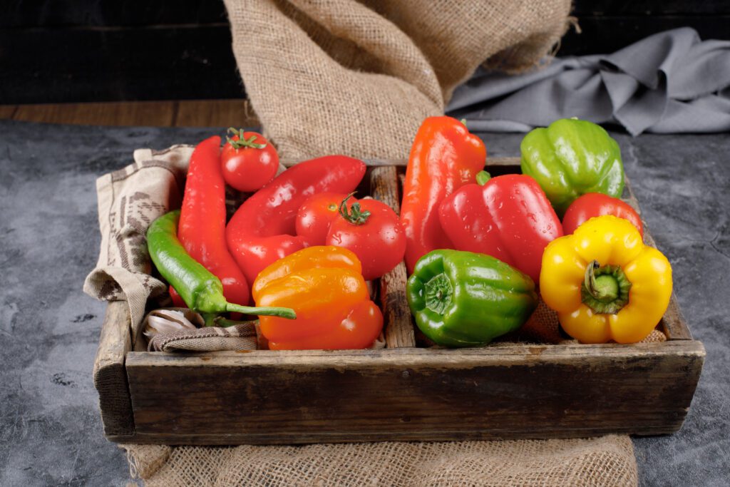 A wooden rustic tray with color peppers and tomatoes inside.